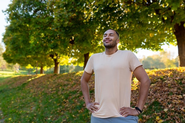 Lächelnder Sportler ruht sich im Park auf einem Lauf, ein Mann atmet frische Luft und genießt einen aktiven Lebensstil