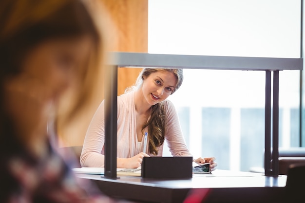 Lächelnder Student, der nahe bei dem Fenster nimmt Kenntnisse sitzt