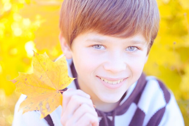 Lächelnder süßer Teenager-Junge mit gelbem Herbstlaub im Freien im Park. Herbstsaison