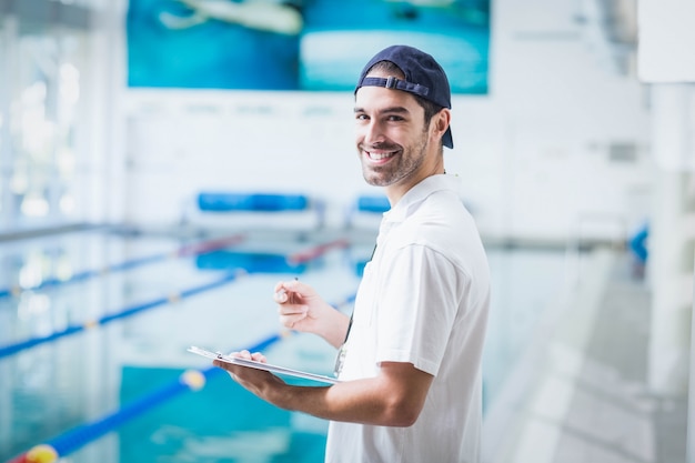 Lächelnder Trainer, der Klemmbrett am Pool hält