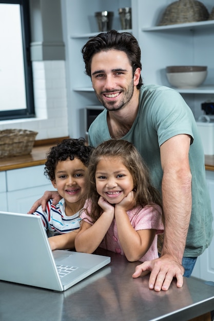 Lächelnder Vater, der Laptop mit seinen Kindern in der Küche verwendet