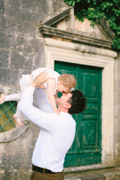 Lächelnder Vater hob seine kleine Tochter in den Armen vor dem Hintergrund der Tür eines alten