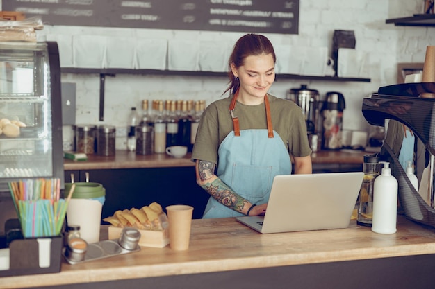 Lächelnder weiblicher Barista mit Notebook im Café