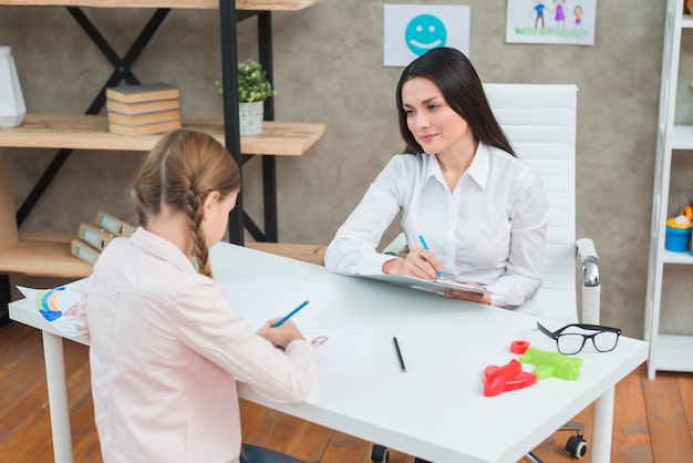 Foto lächelnder weiblicher psychologe, der das mädchen während der therapiesitzung beobachtet