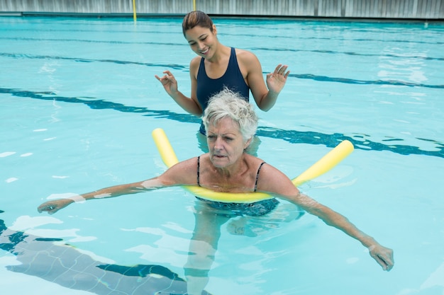 Foto lächelnder weiblicher trainer, der ältere frau im schwimmbad hilft