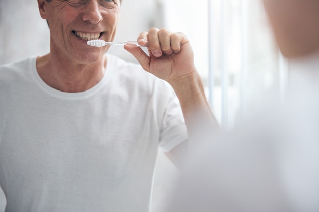 Lächelnder zufriedener reifer Mann, der seine Zähne mit einer Zahnbürste putzt