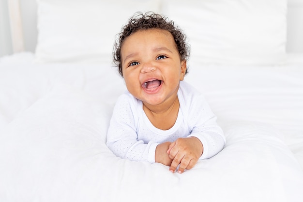 Lächelndes afroamerikanisches kleines Baby auf weißem Bett im Schlafzimmer lachend