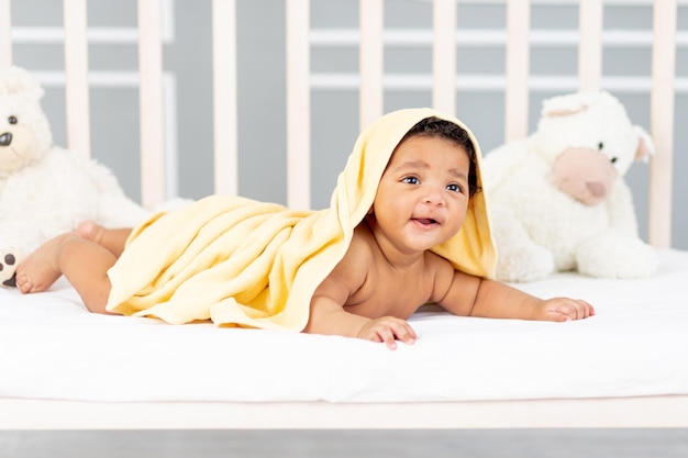 Lächelndes afroamerikanisches kleines Baby liegt nach einem Bad in einem gelben Handtuch im Bett