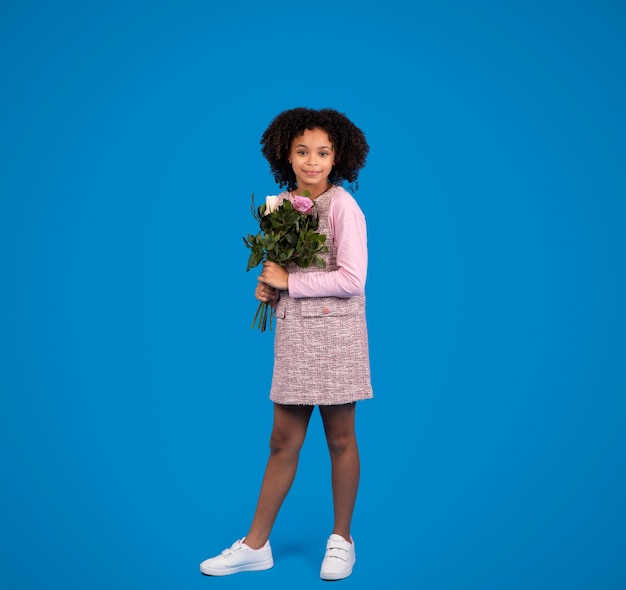 Lächelndes afroamerikanisches kleines Mädchen mit Blumenstrauß isoliert auf blauem Hintergrund