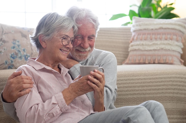 Lächelndes, angenehmes älteres Paar, das sich zu Hause entspannt, auf dem Boden sitzt und sich zärtlich umarmt