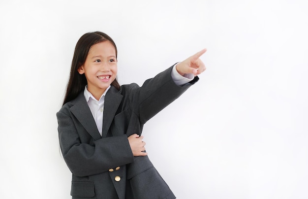 Lächelndes asiatisches kleines Mädchen trägt Business-Anzug und zeigt nach oben isoliert auf weißem Hintergrund