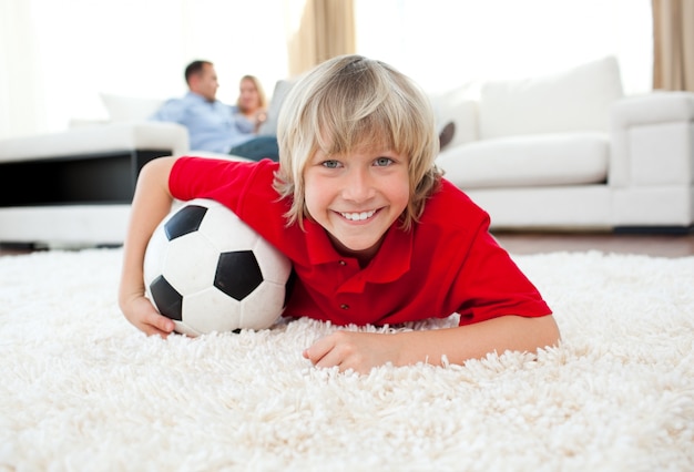 Lächelndes aufpassendes Fußballspiel des Jungen, das auf dem Boden liegt