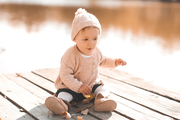 Lächelndes Babymädchen 1-2 Jahre alt, das stilvolle gestrickte Kleidung trägt, die draußen sitzt