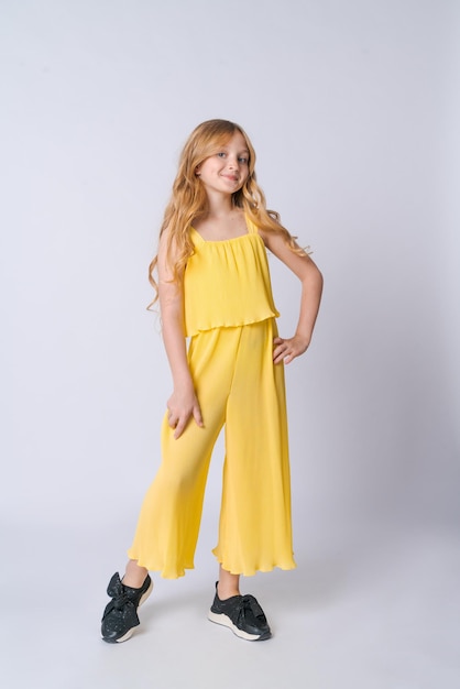 Lächelndes blondes Mädchen im gelben Sommeranzug posiert isoliert auf hellgrau