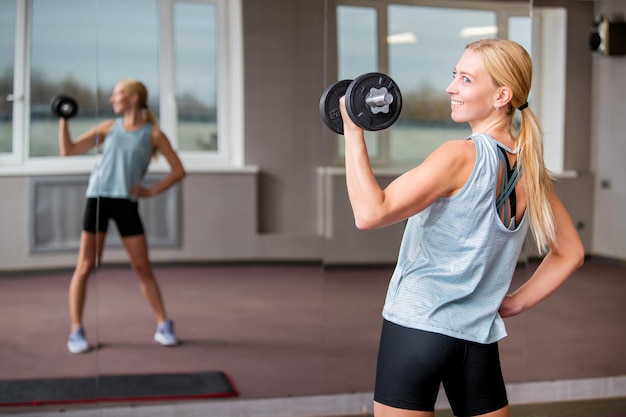 Lächelndes blondes Mädchen macht Übungen mit Hanteln im Fitnessstudio