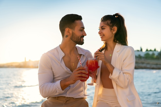 Lächelndes ethnisches Paar, das Cocktails am Ufer trinkt