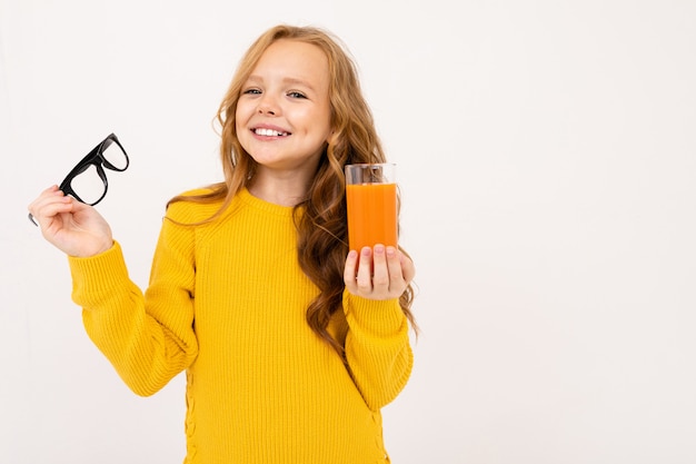 Lächelndes europäisches Mädchen nahm ihre Gläser ab und hält ein Glas Karottensaft in ihrer Hand