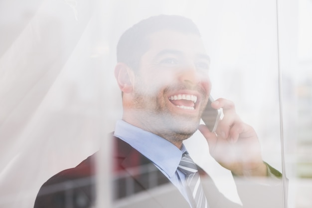 Lächelndes Geschäftsmann heraus Fenster an der Kamera am Telefon