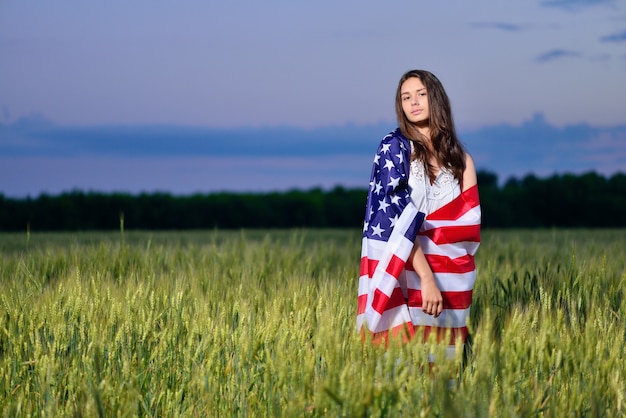 Lächelndes glückliches Mädchen mit der amerikanischen Flagge auf seinen Schultern. 4. Juli - Unabhängigkeitstag