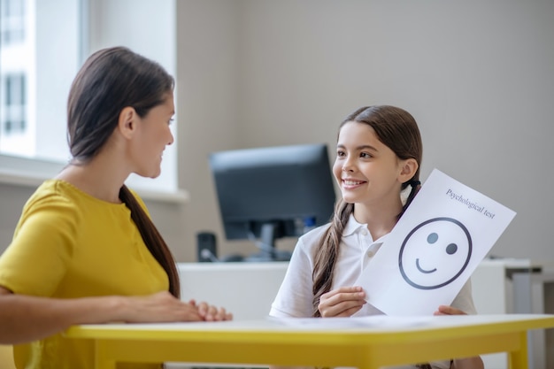 Lächelndes hübsches Mädchen mit langen dunklen Haaren, die positive Emotionszeichnung und glücklichen Psychologen halten