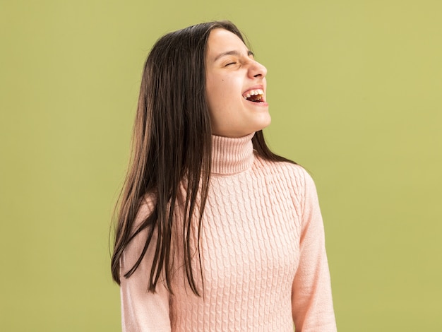 Lächelndes hübsches Teenager-Mädchen, das in der Profilansicht steht und auf die Seite mit offenem Mund schaut, isoliert auf olivgrüner Wand?