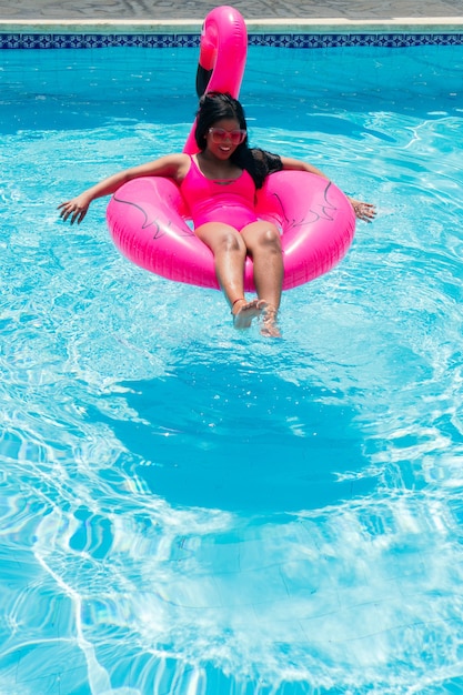 Lächelndes junges afrikanisches Mädchen im Bikini entspannt sich auf aufblasbarem rosa Flamingo im Schwimmbad.