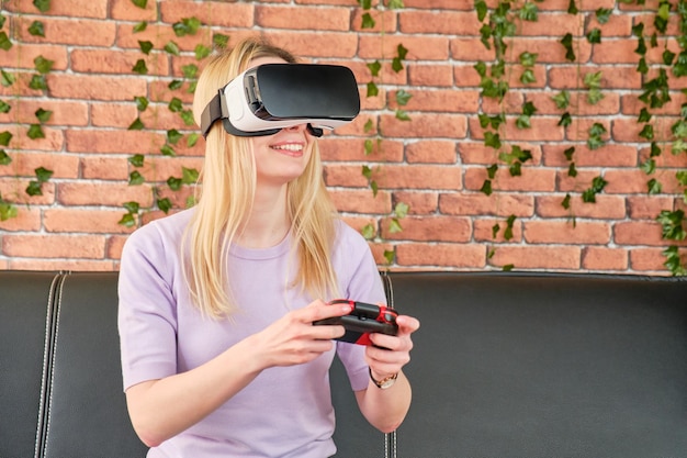 Lächelndes junges blondes Mädchen mit Virtual-Reality-Brille, das ein Videospiel spielt