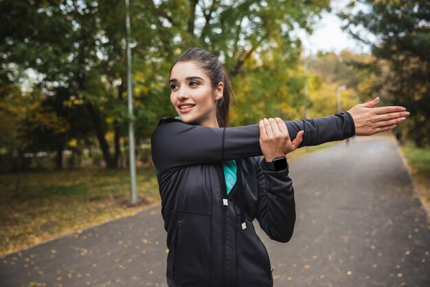 Lächelndes junges Fitnessmädchen, das Übungen im Park macht