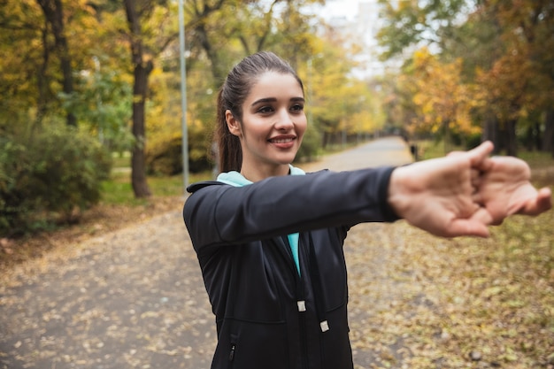 Lächelndes junges Fitnessmädchen, das Übungen im Park macht