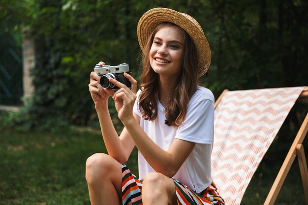 Lächelndes junges Mädchen, das auf einer Hängematte am Stadtpark draußen im Sommer ruht und ein Foto mit Fotokamera macht