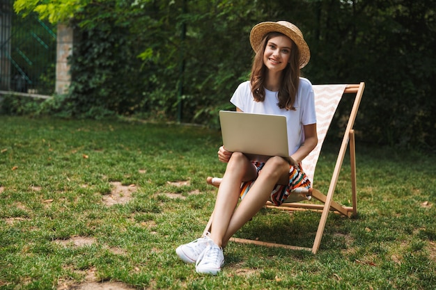 Lächelndes junges Mädchen, das mit Laptop-Computer am Park draußen sitzt