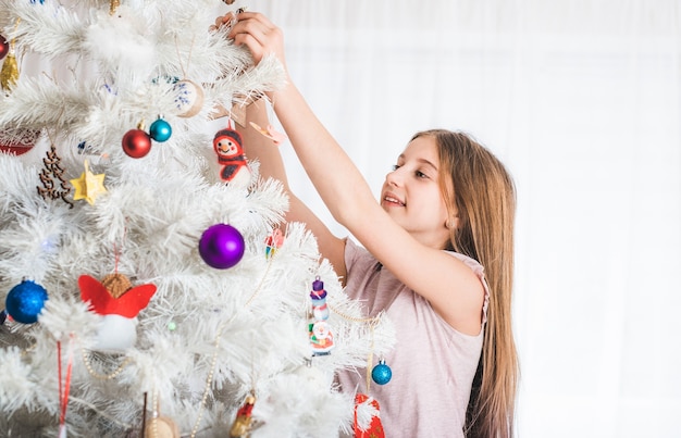 Lächelndes junges Mädchen, das weißen Weihnachtsbaum verziert