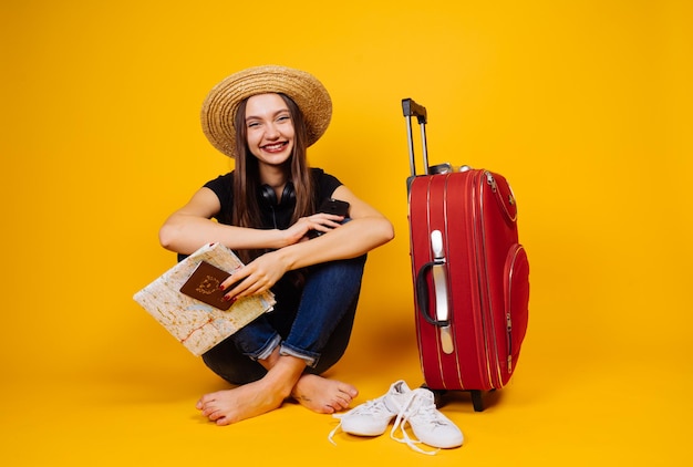 Lächelndes junges Mädchen in einem Strohhut fliegt in den Urlaub und wartet auf eine Sojasauce mit einem großen roten Koffer