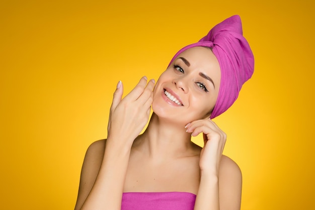 Lächelndes junges Mädchen mit einem rosa Handtuch auf dem Kopf, das ein Spa genießt, saubere Haut