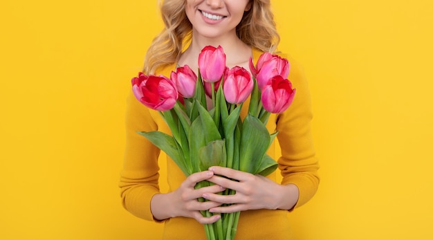 Lächelndes junges Mädchen mit Frühlingstulpenblüten auf gelbem Hintergrund
