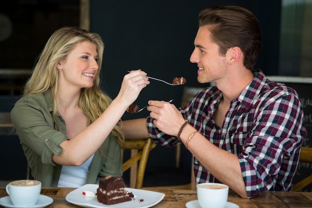 Lächelndes junges Paar, das einander Nachtisch im Café füttert