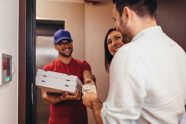 Foto lächelndes junges paar, das zu hause pizza vom lieferboten erhält.