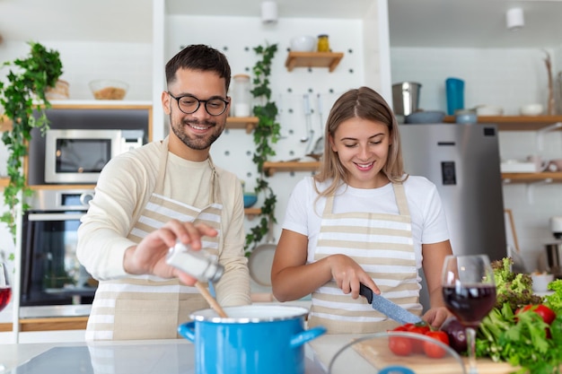 Lächelndes junges Paar, das zusammen in der Küche Essen kocht und eine tolle Zeit zusammen hat Mann und Frau lachen und trinken morgens Milch zum Frühstück