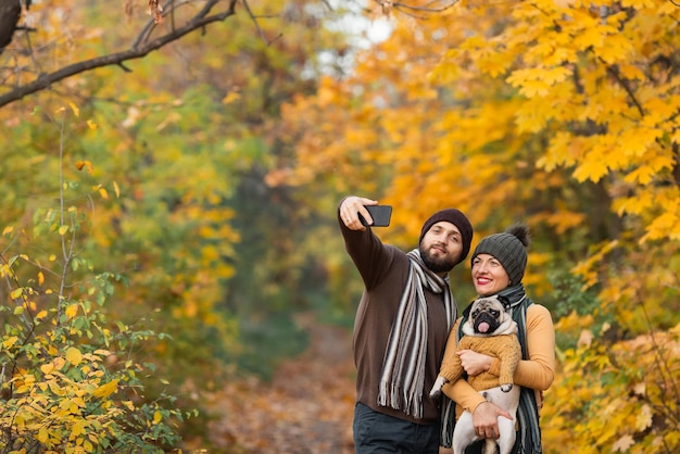 Lächelndes junges Paar mit Hund im Freien im Herbstpark, der Selfie macht