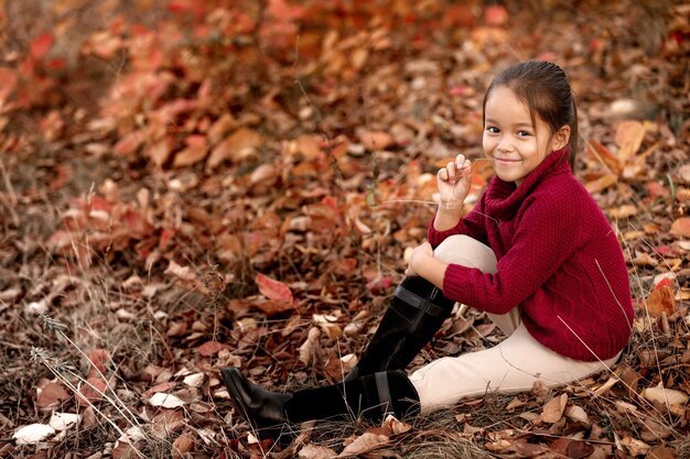 Lächelndes Kind 5 Jahre alt, das im Herbstpark aufwirft. kleines Mädchen, das in gefallenen Blättern sitzt. glückliche Kindheit