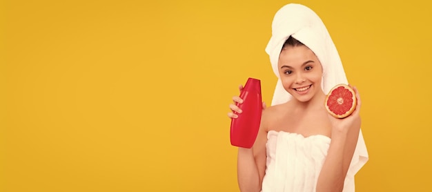 Lächelndes Kind im Handtuch mit Grapefruit-Shampoo-Flasche auf gelbem Hintergrund Kosmetik und Hautpflege für Teenager-Kind-Plakat-Design Beauty Kid Girl Banner mit Kopierbereich