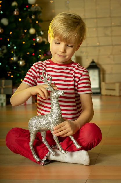 Foto lächelndes kind in einer roten weihnachtsmannmütze, die mit silberhirsch spielt