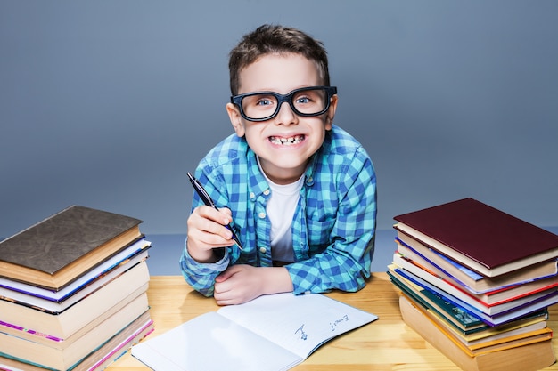 Lächelndes Kind in Gläsern, die Hausaufgaben am Schreibtisch machen. Junger Schüler im Klassenzimmer