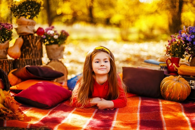 Lächelndes Kind mit Korb der roten Äpfel, die im Herbstpark sitzen