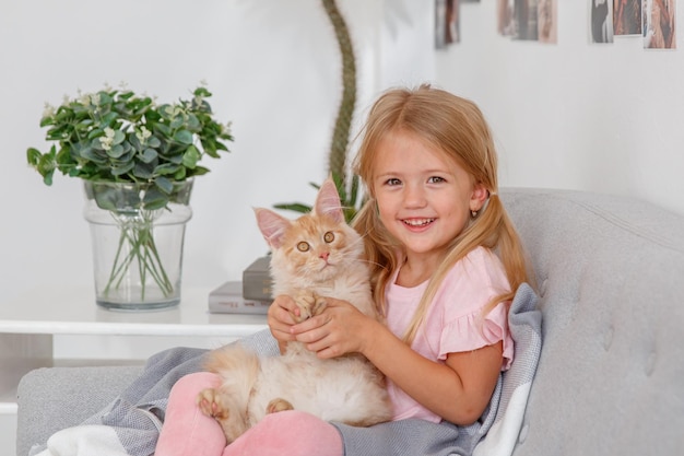 Lächelndes Kindermädchen, das auf dem Sofa sitzt, umarmt Katze