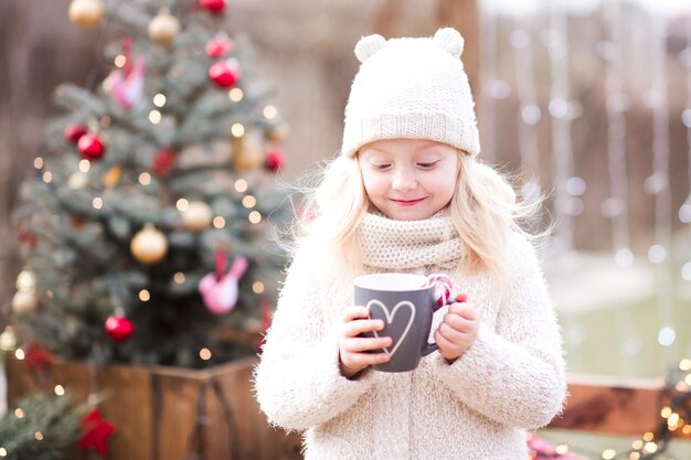 Lächelndes Kindermädchen, das draußen Tee über dem Weihnachtsbaum trinkt