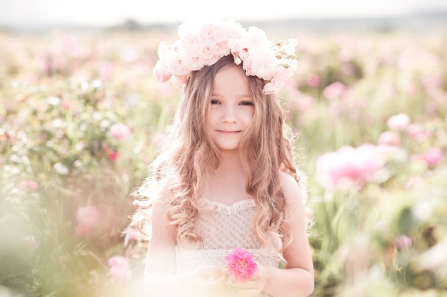 Lächelndes Kindermädchen, das eine Rosenblume auf der Wiese im Freien hält