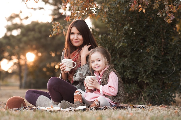 Lächelndes Kindermädchen, das mit der Mutter sitzt und heißen Tee im Park trinkt?