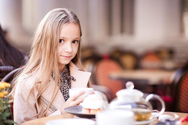 Lächelndes Kindermädchen, das Tee im Café im Freien trinkt