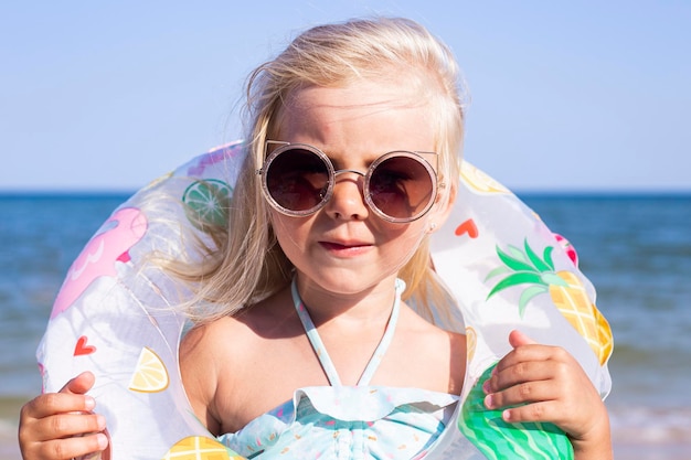 Lächelndes Kindermädchen mit Sonnenbrille mit einem Gummiring am Strand.